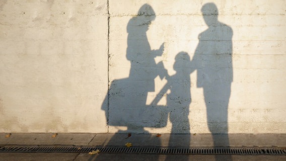 The shadows of a woman, a child and a man in front of a wall.  © photocase.de Photo: krockenmitte