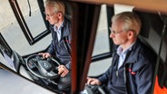 Ein Fahrer der Verkehrsgesellschaft Rheinbahn ist im Rückspiegel zu sehen, während er einen Bus durch die Stadt steuert. © picture alliance Foto: Oliver Berg