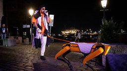 Ein Rapper der Band "Deichkind" führt einen Roboter-Hund an der Leine. © NDR/ Morris Mac Matzen Foto: Morris Mac Matzen