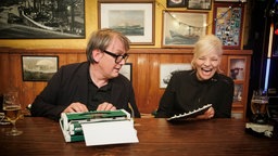 Ina Müller lacht während Sven Regener neben ihr auf einer kleinen Schreibmaschine schreibt. © NDR/ Morris Mac Matzen Foto: Morris Mac Matzen