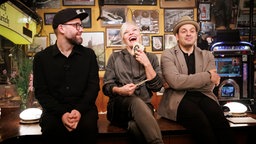 Ina Müller sitzt bei Inas Nacht lachend mit Mark Forster und Kaya Yanar auf dem Tresen. © NDR/ Morris Mac Matzen Foto: Morris Mac Matzen