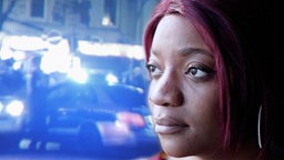 Elisabeth M. vor einem Hintergrund aus Polizeifahrzeugen mit Blaulicht. © NDR / ARD 