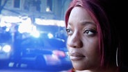 Elisabeth M. vor einem Hintergrund aus Polizeifahrzeugen mit Blaulicht. © NDR / ARD 