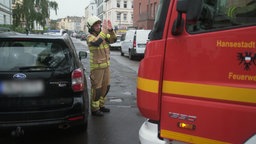 Ein Feuerwehrmann dirigiert ein Feuerwehrfahrzeug durch eine zugeparkte Straße in Lübeck. © NDR 