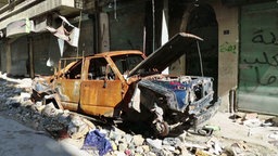 Ein ausgebranntes Autowrack in einer zerstörten Straße in Aleppo. © NDR/ARD 