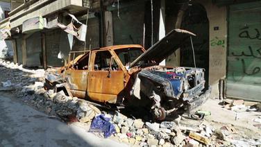 Ein ausgebranntes Autowrack in einer zerstörten Straße in Aleppo. © NDR/ARD 