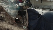 Eine Frau kocht in dem Flüchtlingslager Kara Tepe etwas am Feuer © ARD/NDR Foto: Screenshot