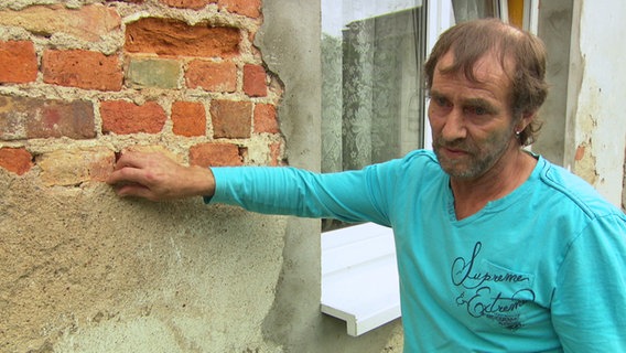 Roman Benter zeigt auf Risse in der Mauer.  