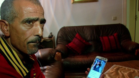 Salah T. hält ein Telefon mit dem Foto seines Sohnes in der Hand.  
